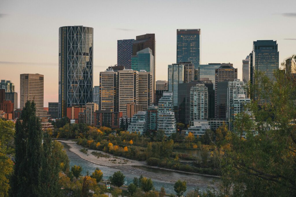 Image is of the Calgary skyline with the Bow River in the foreground. The light looks like the image was taken at sunset and the leaves suggest it is fall.